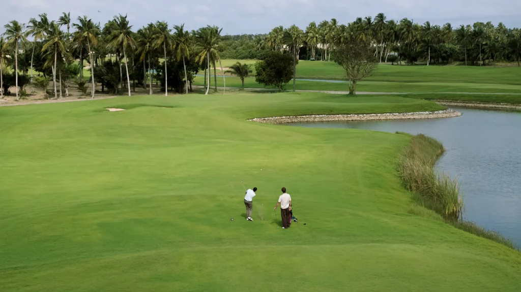Deux golfeurs sur un fairway bordé d’un plan d’eau et de cocotiers