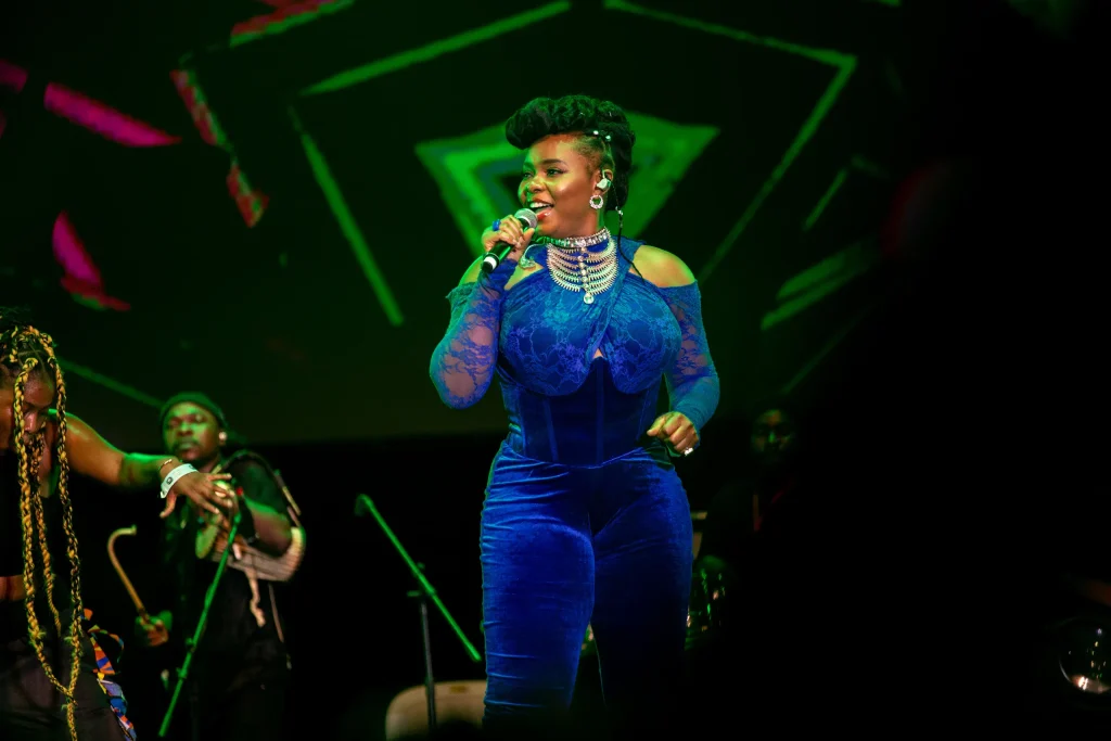 Une chanteuse en tenue bleue, micro en main, sur scène avec ses musiciens dans une lumière verte